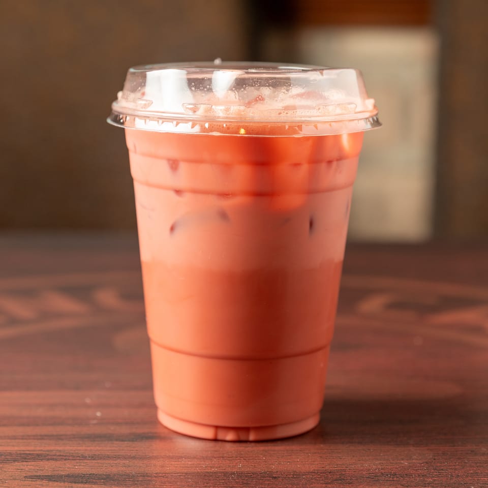 Iced pink beverage in a clear plastic cup with a domed lid, sitting on a warmly lit wooden table.