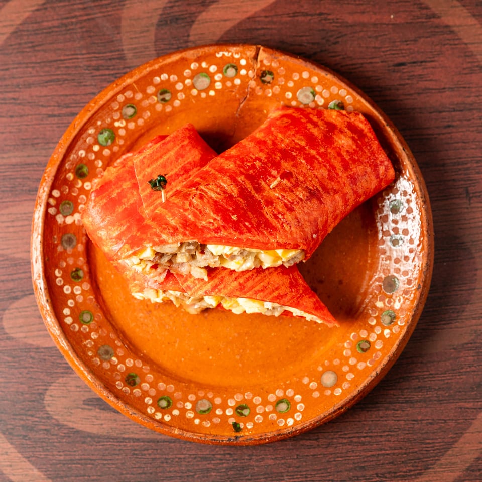 Two red-orange stuffed tortillas filled with shredded meat and melted cheese, served on a decorative ceramic plate.
