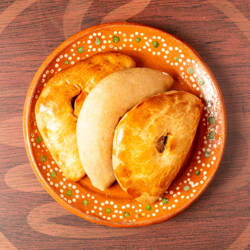 Assorted golden baked pastries arranged on a colorful ceramic plate atop a wooden table.