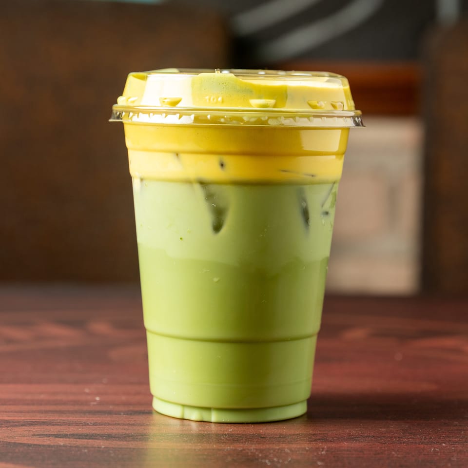 Layered green iced beverage in a clear plastic cup with a domed lid, standing on a wooden table.
